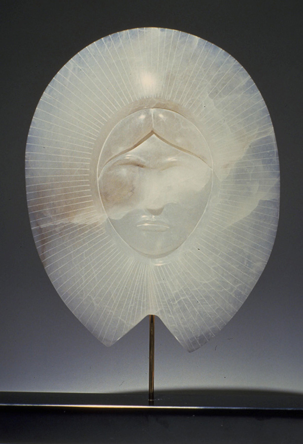Sculpture en albâtre montrant un visage de femme au milieu de rayons de soleil. 
