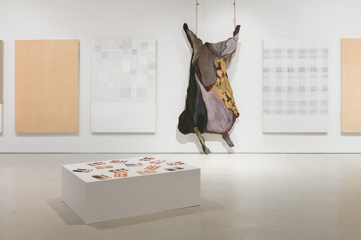Œuvre d’art montrant des canevas suspendus au mur et une table où se trouvent de mini-canevas dans une salle d’exposition. 