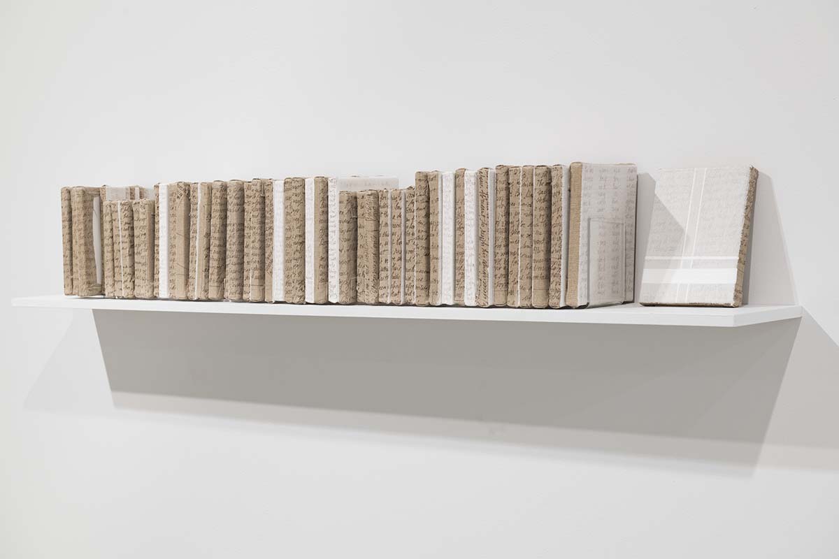 46 petits canevas recouverts de plâtre alignés comme des livres sur une tablette. 