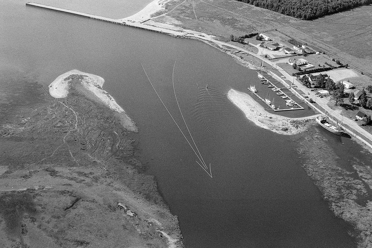 Photo aérienne en noir et blanc montrant un motif de flèche géant dans une rivière. 