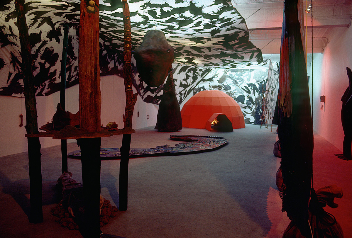 Une toile figurant une canopée noir et blanc est suspendue au-dessus d’un igloo orange, qui est entouré de plusieurs troncs d’arbres minces et de divers objets thématiques. 