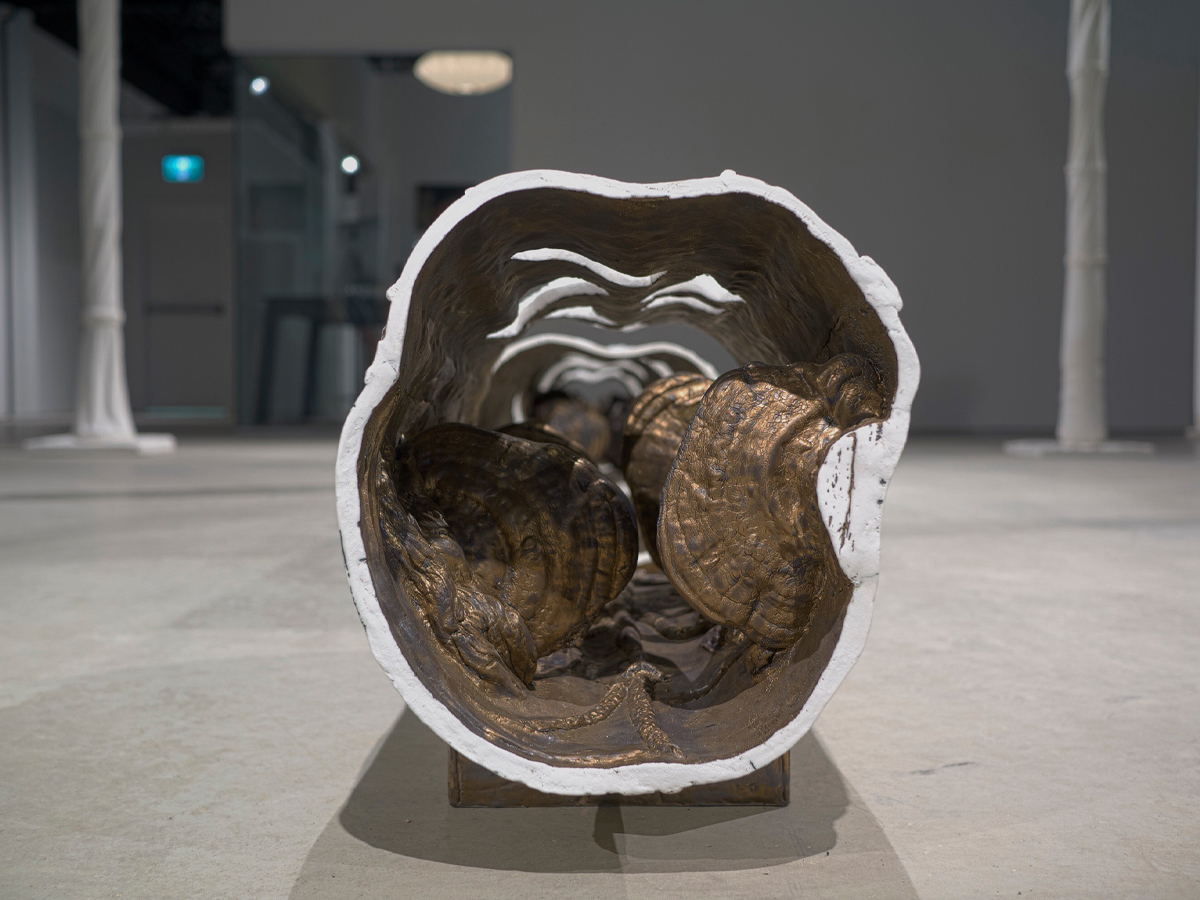 Vue en coupe d’une sculpture de porcelaine représentant une série de billes de bois évidées, à l’intérieur desquelles des formations recouvertes de glaçure métallique évoquent des champignons à chapeau. 