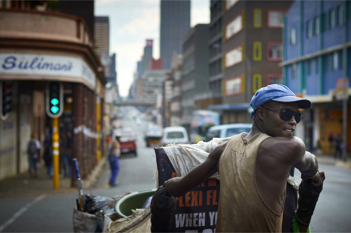Un homme portant un chandail sans manches et une casquette bleue regarde par-dessus son épaule pendant qu’il marche dans une rue de centre-ville. 