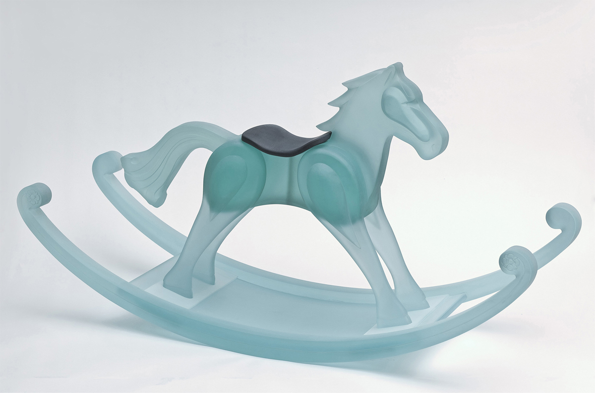 Cheval à bascule de format réel fait en morceaux de verre translucide nettoyé au jet de sable. Le cheval est de couleur turquoise et porte une selle contrastante noire.  