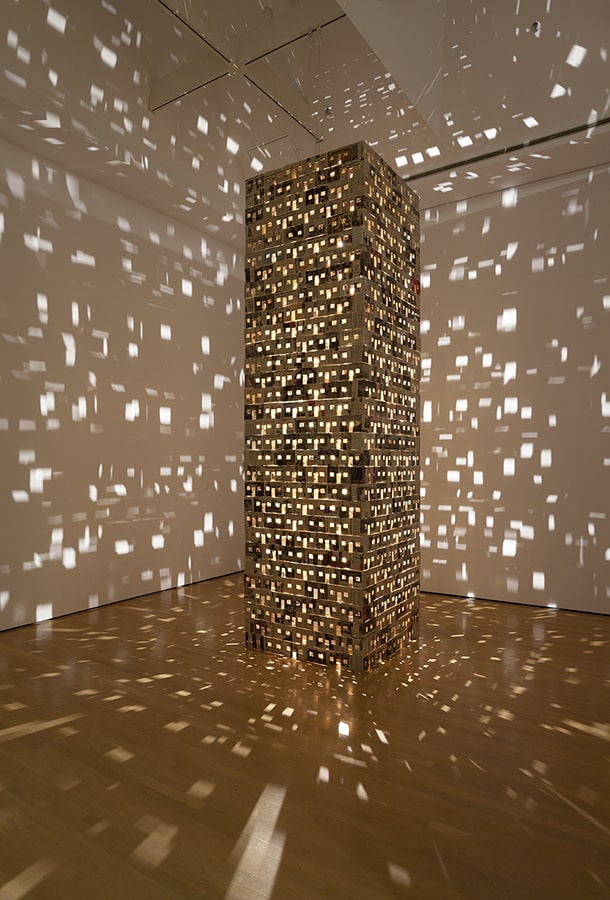 Tour illuminée de l’intérieur qui projette des formes sur les murs autour d’elle. 