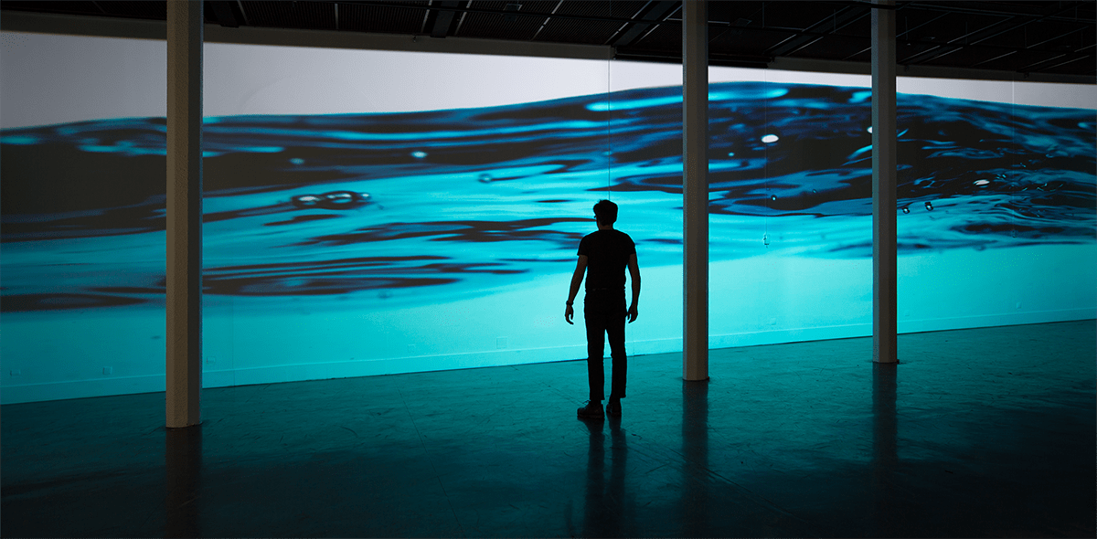 Photo d’un homme en silhouette devant une projection d’eau bleue.  